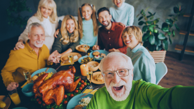 Untitled design (3) Smiling multigenerational family — grandparents, parents, and children with a dog — walking on a sunny beach, symbolizing snowbirds traveling with peace of mind and connected healthcare
