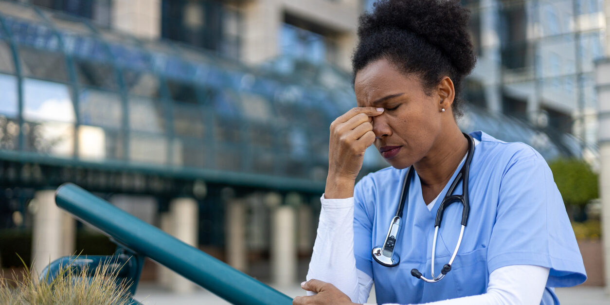 Exhausted and stressed nurse suffering from headache near hospital