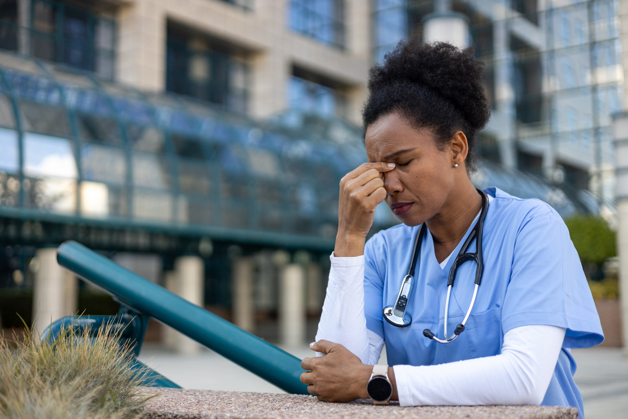 Exhausted and stressed nurse suffering from headache near hospital